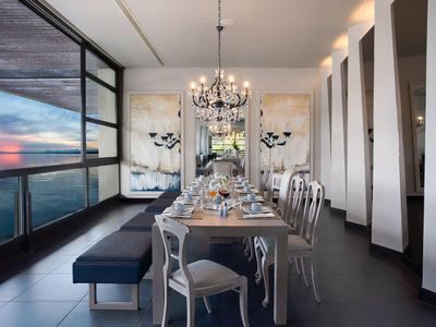 Moderner Essbereich mit langem Holztisch, weißen Stühlen, Kronleuchter und großem Fensterblick.