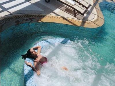 Frau entspannt im Whirlpoolbereich eines Hallenbads mit Liegestühlen und Sonneneinstrahlung.