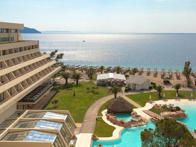 Hotel met zwembad, palmbomen en direct uitzicht op de zee op een zonnige dag.