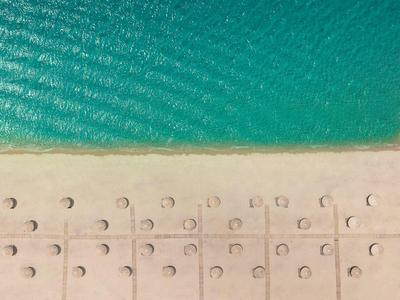 Blick aus der Vogelperspektive auf einen Strand mit Reihen von Sonnenschirmen und türkisfarbenem Meer.