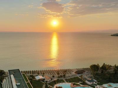Sonnenuntergang über ruhigem Meer mit Strand, Pools und Gebäuden im Vordergrund.