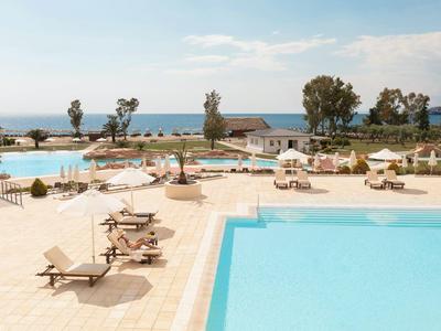 Großer Hotelpool mit Liegestühlen und Blick auf das Meer bei sonnigem Wetter.