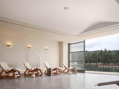 Heller Ruheraum mit Holzliegen, wandmontierten Lampen und großen Fenstern mit Blick ins Grüne.