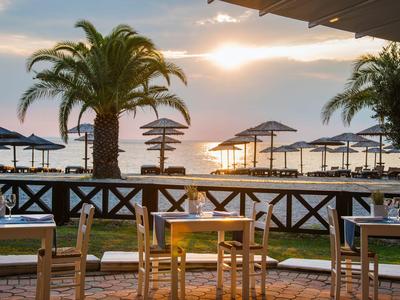 Strandrestaurant mit Tischen und Stühlen, Palmen und Sonnenschirmen bei Sonnenuntergang