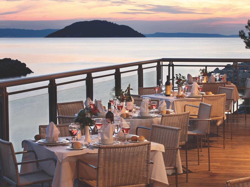 Terrassenrestaurant am Meer mit gedeckten Tischen und Blick auf Inseln bei Sonnenuntergang.