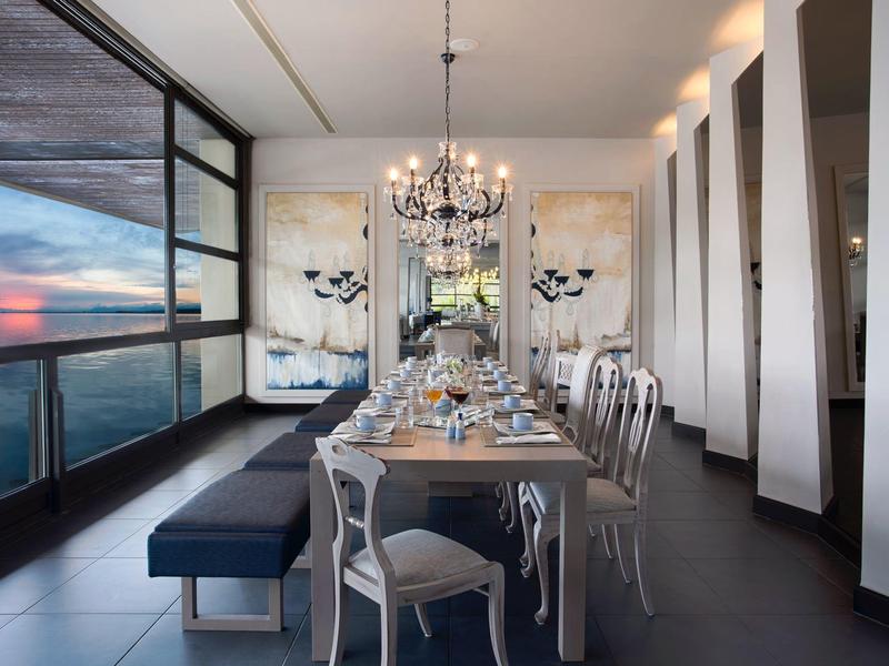 Moderner Essbereich mit langem Holztisch, weißen Stühlen, Kronleuchter und großem Fensterblick.