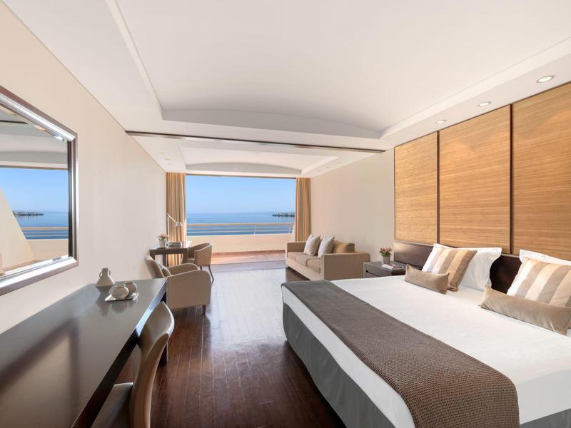 Modern eingerichtetes Hotelzimmer mit Doppelbett, großem Fensterblick auf das Meer und Holzdetails.