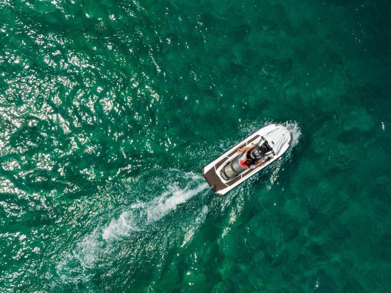 Ein kleines Boot fährt über das türkisfarbene Meerwasser, von oben betrachtet.