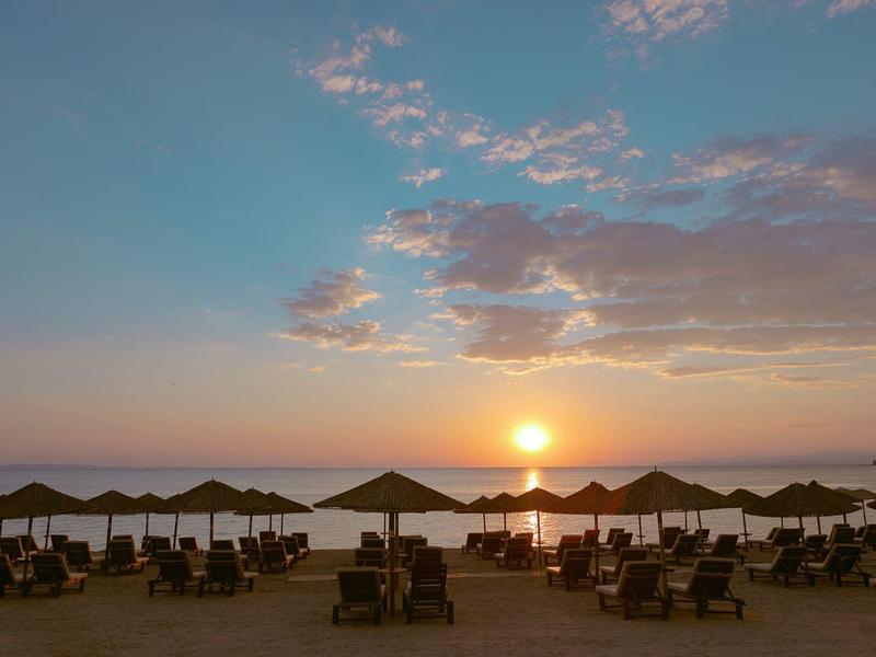 Strand mit Sonnenschirmen und Liegestühlen bei Sonnenuntergang über ruhigem Meer.