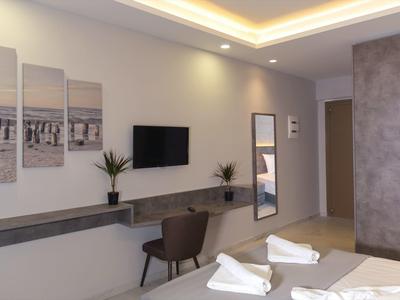 Modernes Schlafzimmer mit grauen Wänden, Wand-TV, Spiegel, Schreibtisch und zwei Handtüchern auf dem Bett.