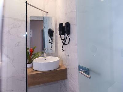 Badezimmer mit rundem Waschbecken, hölzernem Regal, Wandspiegel und Wand-Haartrockner in weißem Marmor.