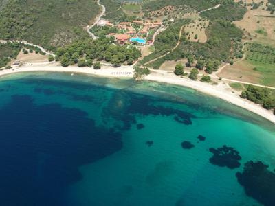 Luftaufnahme einer Bucht mit klarem, blaugrünem Wasser und einem langen Sandstrand, umgeben von grüner Landschaft.