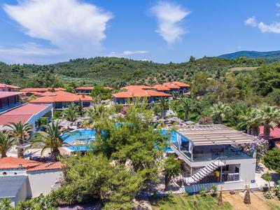 Hotelanlage mit Pool in tropischer Umgebung und Bergen im Hintergrund unter blauem Himmel.