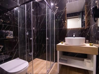 Modernes Badezimmer mit schwarzer Marmorwand, Glasdusche, weißer Toilette und Holzwaschtisch.