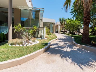 Moderner Hotelbereich mit Garten, Palmen und geschwungener Steinmauer bei Sonnenschein.