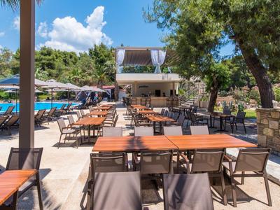 Freiluftrestaurant mit Holztischen und Stühlen unter Bäumen an sonnigem Tag.