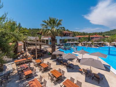 Hotelpool mit Liegestühlen, Sonnenschirmen und Essbereich unter Palmen bei sonnigem Himmel.