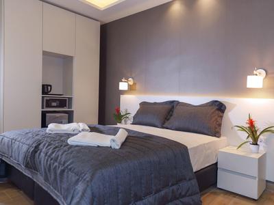 Modern eingerichtetes Schlafzimmer mit grauem Bett, weißen Schränken und Nachttischen, warmes Licht.