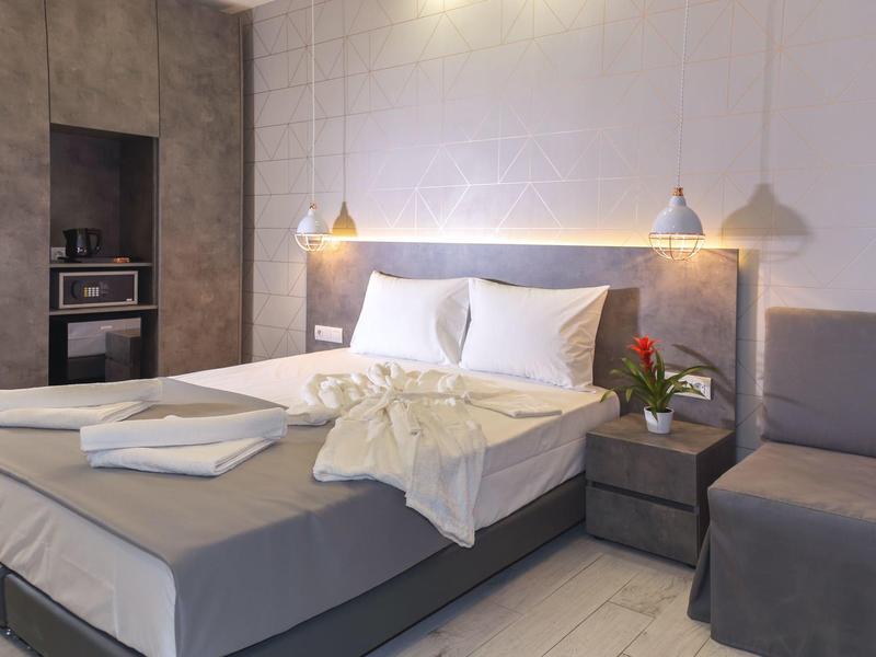 Modernes Schlafzimmer mit grauem Bett, weißen Bettdecken, grauem Sessel und zwei Hängeleuchten.