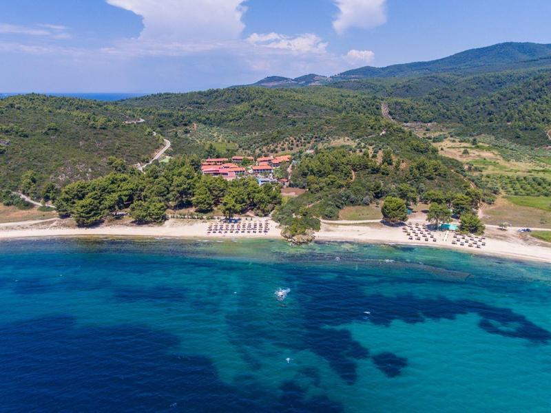Küstenlinie mit Sandstrand, klarem blauem Wasser und grünen Hügeln im Hintergrund.