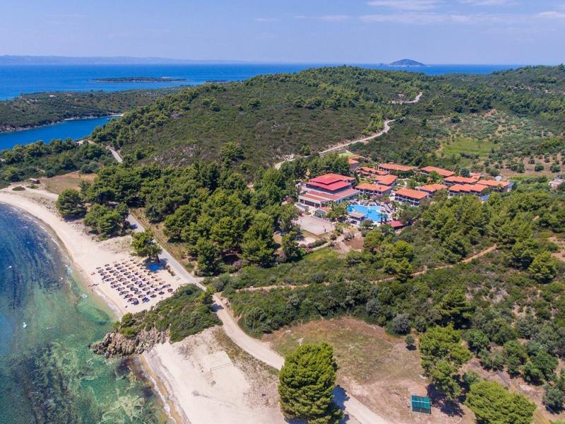 Luftaufnahme einer Küstenlandschaft mit klarem blauem Meer, Sandstrand und bewaldetem Hügel.