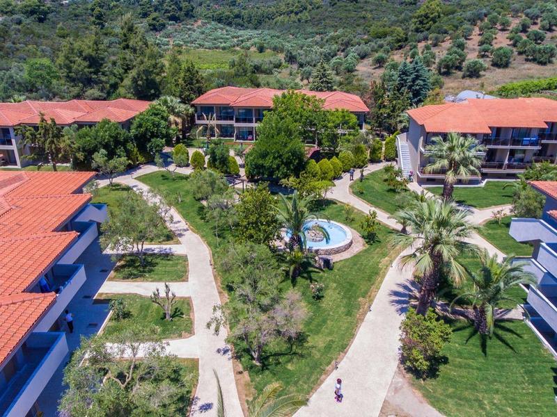 Luftaufnahme eines Ferienresorts mit roten Dächer, Wegen, Bäumen und Hügeln im Hintergrund.