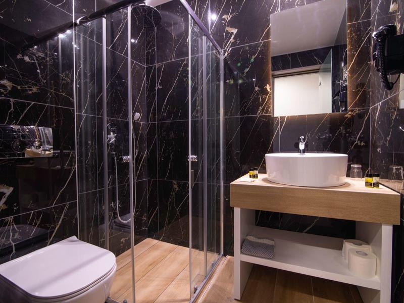 Modernes Badezimmer mit schwarzer Marmorwand, Glasdusche, weißer Toilette und Holzwaschtisch.