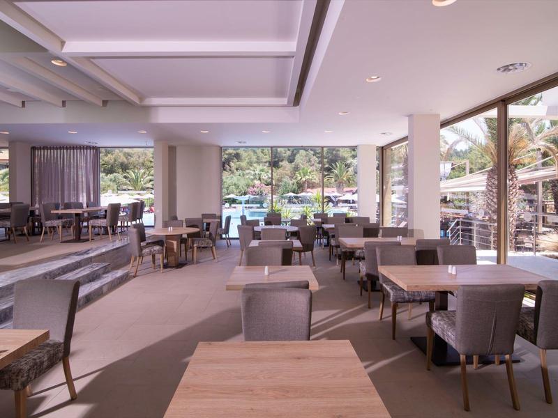 Großes Café mit vielen Tischen, Stühlen und großen Fenstern, die den Blick ins Grüne freigeben.