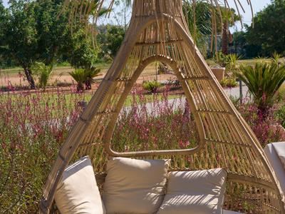 Gemütlicher runder Korbsessel mit Kissen im Außenbereich bei Sonnenschein.