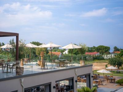 Terrassengarten mit Tischen, Stühlen und Sonnenschirmen über einem Gebäude bei klarem Himmel.