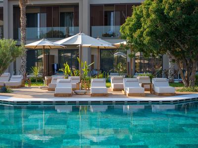 Hotelpool mit Liegestühlen und Sonnenschirmen vor einem Gebäude mit Balkonen.