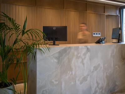 Modern reception desk with marble facade, wood paneling, subtle lighting, and a plant.
