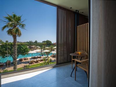 Balcony with chair and table overlooking swimming pool and palm trees under clear sky.