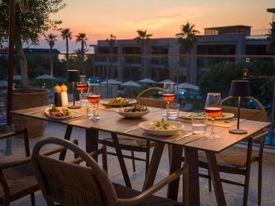 Abendessen auf einer Terrasse mit Blick auf einen beleuchteten Pool und Palmen bei Sonnenuntergang.