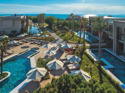 Hotelanlage mit Pools, Liegestühlen und Sonnenschirmen entlang eines gepflegten Weges zum Meer.