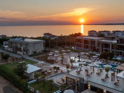 Sunset over a modern hotel with pool and gardens by the sea.