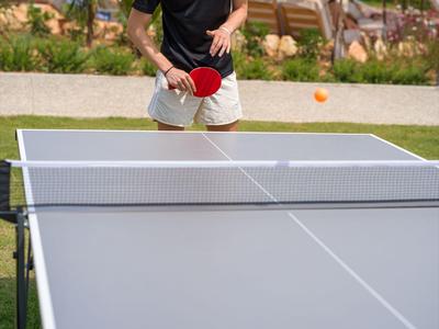 Mann spielt Tischtennis im Freien neben Hotel mit Sonnenschirmen und Liegestühlen.