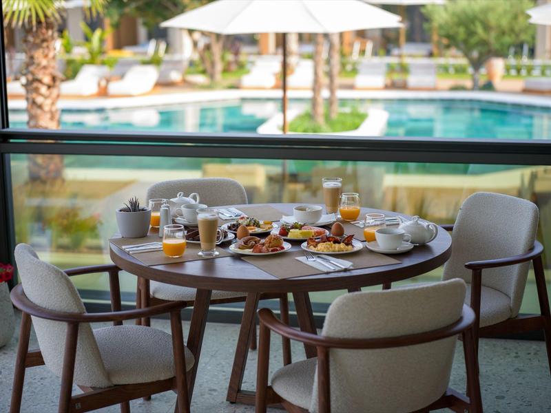 A set breakfast table on a terrace overlooking a pool with umbrellas.