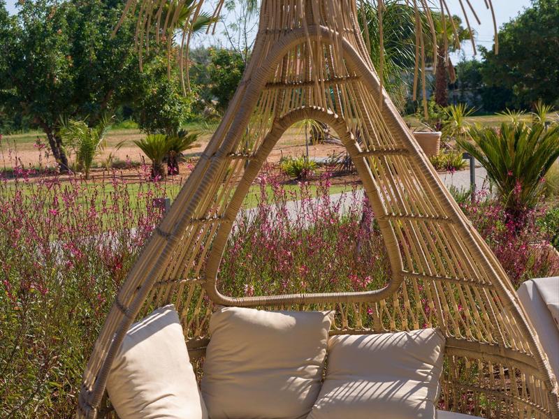Round hanging rattan seat with cushions in a sunny garden setting.