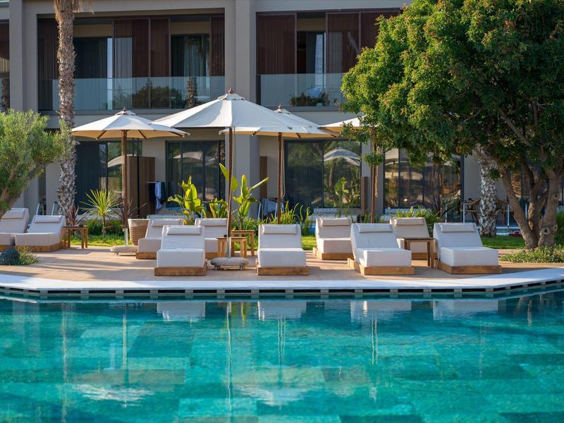 Pool area with lounge chairs and umbrellas in front of a hotel building