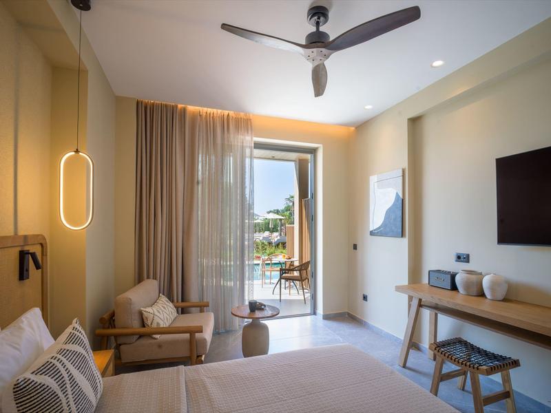Modern hotel room with balcony, light furniture, and ceiling fan.