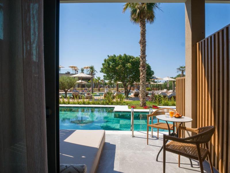 View from a hotel terrace overlooking a pool with garden and sun umbrellas in the background.
