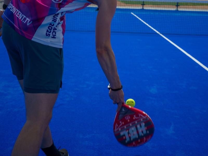 Person holding a padel racket preparing to serve on a blue padel court