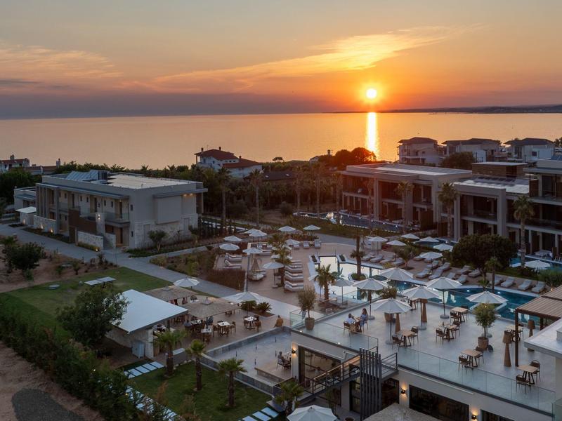 Sunset over a modern hotel with pool and gardens by the sea.