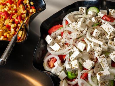 Salát s fetou a zeleninou vedle kukuřičného jídla v černých miskách.