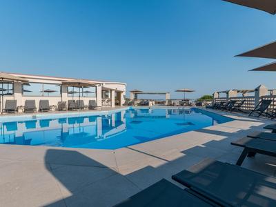 Terrassenbereich eines Hotels mit modernen Stühlen und Tischen, Blick auf grüne Bäume und blaues Meer.