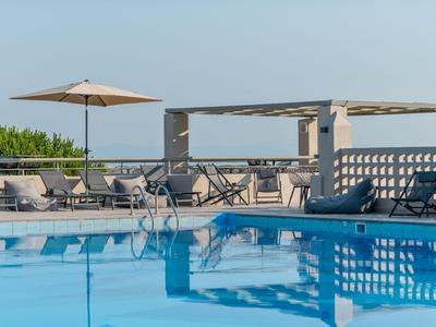 Blick auf einen klaren Außenpool mit Liegestühlen und Sonnenschirm bei klarem Himmel.