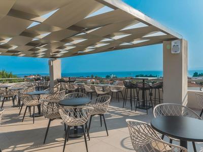 Dachterrasse mit Tischen und Stühlen, Blick auf das Meer bei klarem Himmel.