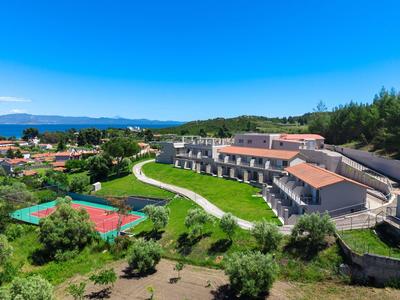 Kompleks hotelowy z czerwonym kortem tenisowym, otoczony zielonym krajobrazem i górami w tle.