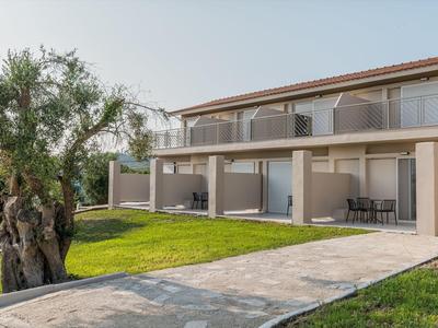 Modernes Hotelgebäude mit Terrasse, Garten und altem Baum im Vordergrund.